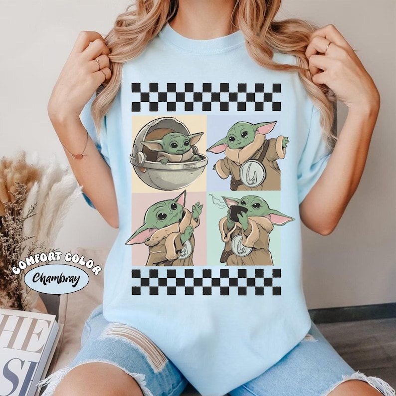 Pode incluir: Camiseta azul claro com um design de quatro pain&eacute;is com imagens de um personagem alien&iacute;gena verde. Os pain&eacute;is s&atilde;o emoldurados por padr&otilde;es de xadrez em preto e branco. O texto "COMFORT COLOR Chambray" &eacute; impresso na camiseta.