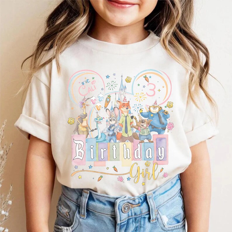 May include: A beige t-shirt with a colourful graphic of animated movie characters, a castle, and the words "Birthday Girl". The number "3" is also displayed. The shirt is worn by a child.