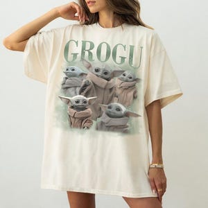 Puede incluir: Camiseta color crema con la palabra "GROGU" en verde sobre un gr&aacute;fico de Grogu de The Mandalorian. El gr&aacute;fico muestra a Grogu en varias poses, con una capa marr&oacute;n, con un fondo verde claro.