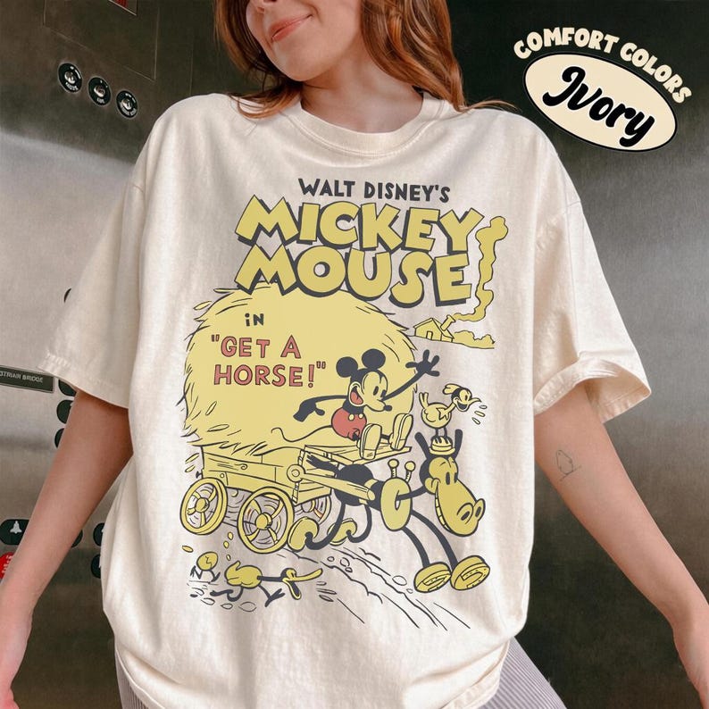 May include: Ivory-colored t-shirt featuring a vintage Mickey Mouse graphic from the film "Get a Horse!". The design includes Mickey, a horse, and a wagon in a classic cartoon style. The shirt is labeled "Comfort Colors".