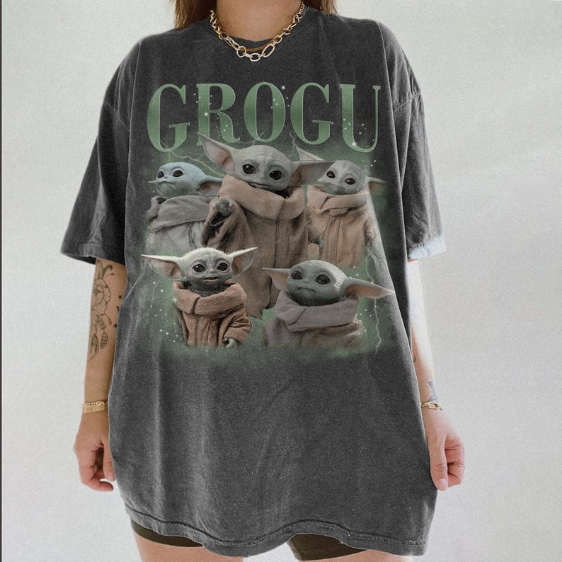 Puede incluir: Camiseta gris oscuro con la palabra "GROGU" en verde sobre un gr&aacute;fico de Grogu, tambi&eacute;n conocido como Baby Yoda, de The Mandalorian. El gr&aacute;fico muestra a Grogu en varias poses, vistiendo un abrigo marr&oacute;n.