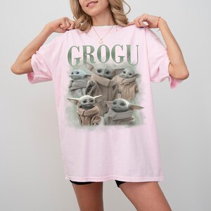 Puede incluir: Camiseta rosa claro con la palabra "GROGU" en letras verdes. Debajo, un gr&aacute;fico de Grogu, el personaje de Star Wars, en varias poses. La camiseta es de estilo casual.