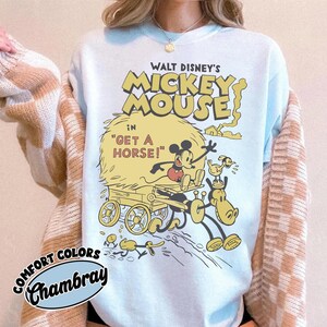May include: Light blue sweatshirt featuring a vintage Mickey Mouse graphic from "Get a Horse!". The design includes Mickey Mouse, a horse, and a hay cart in yellow and black. The text "WALT DISNEY'S MICKEY MOUSE" is above the graphic.