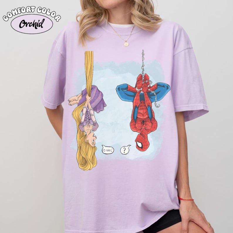 Op de afbeelding: Een lichtpaars Comfort Colors Orchid T-shirt met een cartoonillustratie van Rapunzel en Spider-Man die ondersteboven hangen. Rapunzel houdt haar lange blonde haar vast en Spider-Man hangt aan een web. Spraakballonnen met "O HAI!" en een vraagteken.