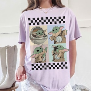 Pode incluir: Camiseta lil&aacute;s claro com um design de quatro pain&eacute;is apresentando um personagem alien&iacute;gena verde. Os pain&eacute;is s&atilde;o definidos em fundos pastel e emoldurados por um padr&atilde;o quadriculado em preto e branco. O alien&iacute;gena &eacute; retratado em v&aacute;rias poses.