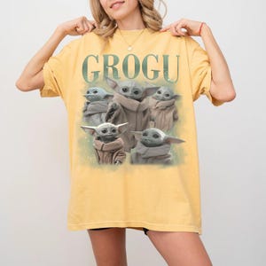 Puede incluir: Camiseta amarilla mostaza con la palabra "GROGU" en verde sobre un gr&aacute;fico de Grogu, tambi&eacute;n conocido como Baby Yoda, de la serie Star Wars. El gr&aacute;fico muestra a Grogu en varias poses. La camiseta es de color liso.