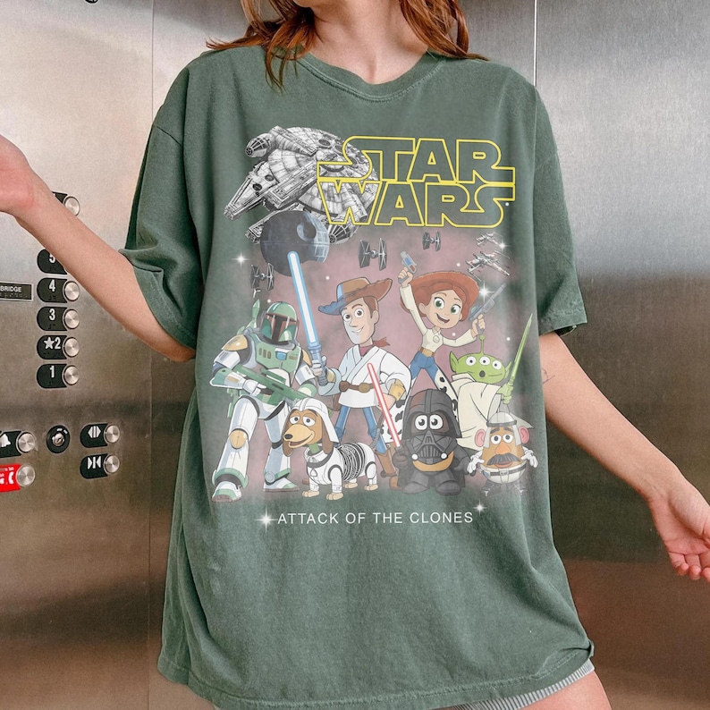 May include: Green t-shirt with a Star Wars graphic, including the text "STAR WARS" in yellow. The design features characters from Star Wars and Toy Story. The words "ATTACK OF THE CLONES" are also visible.