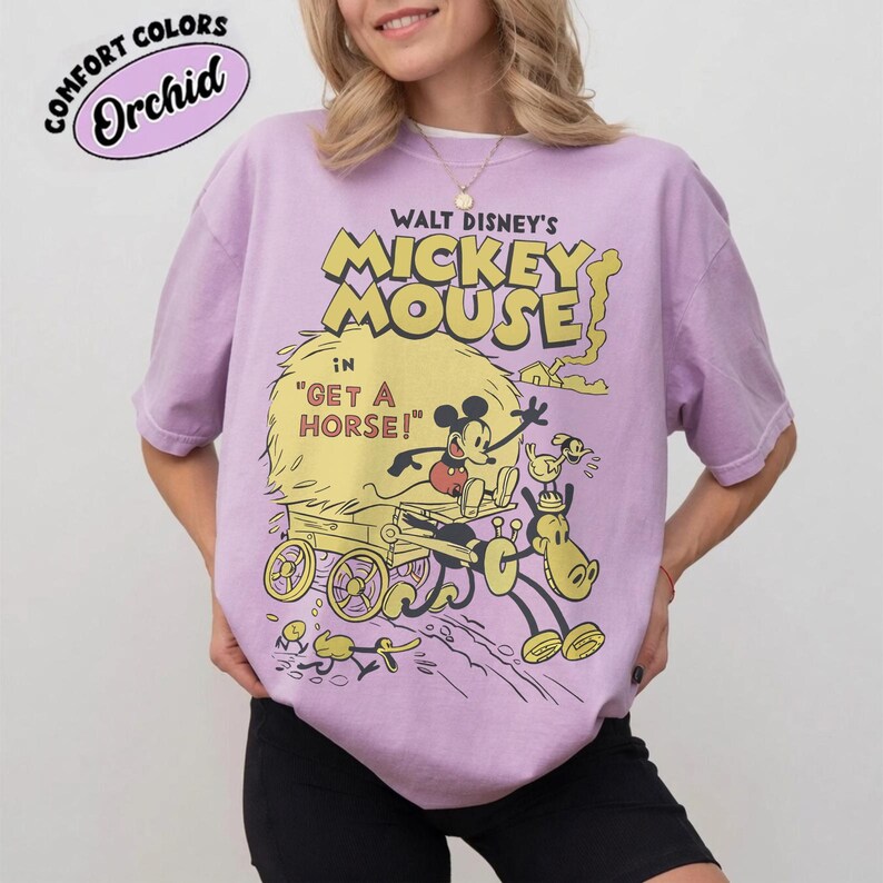 May include: A lilac-colored t-shirt featuring a vintage Walt Disney's Mickey Mouse graphic. The design includes Mickey Mouse, a horse, and the text "Get a Horse!". The shirt has a relaxed fit and the words "Comfort Colors" and "Orchid" are printed on the top left.