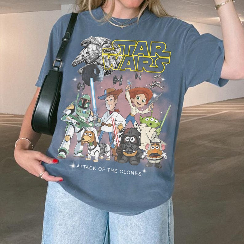 May include: Blue t-shirt with a Star Wars and Toy Story mashup graphic. The design includes the text "STAR WARS" and "ATTACK OF THE CLONES", featuring various characters from both franchises.