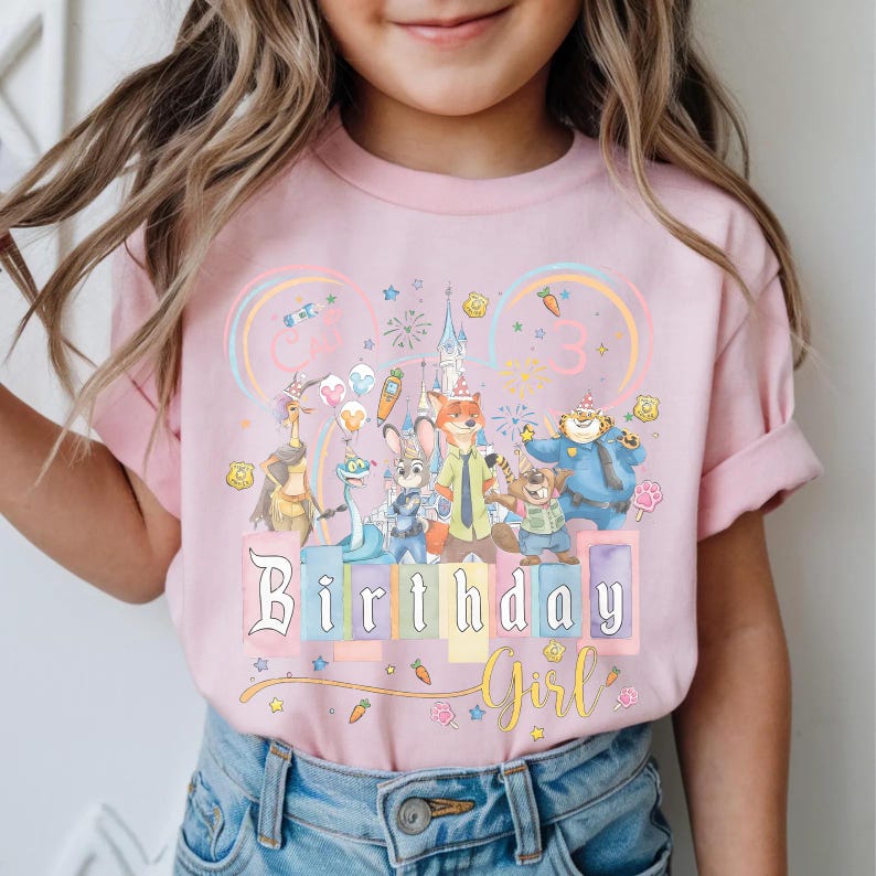 May include: Pale pink t-shirt with a colourful graphic of cartoon characters, a castle, and the words "Birthday Girl." The design includes a rainbow, stars, and the number "3."