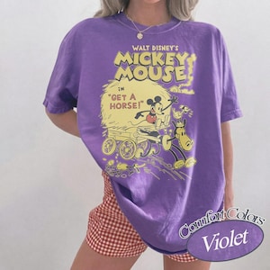 May include: A violet Comfort Colors t-shirt featuring a vintage Walt Disney's Mickey Mouse graphic. The graphic includes Mickey Mouse, a horse, and the text "Get a Horse!". The shirt has a crew neck and short sleeves.