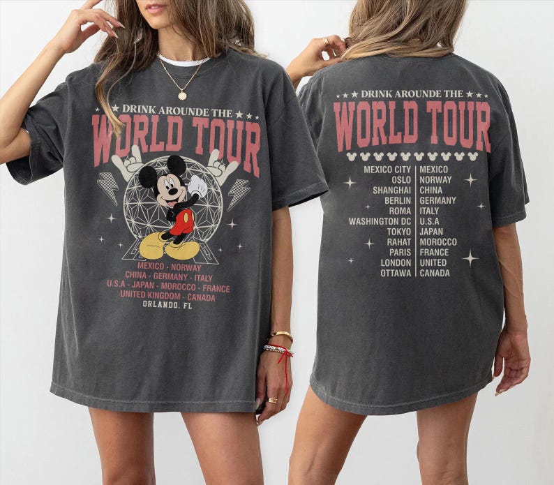 K&ouml;nnte beinhalten: Dunkelgraues T-Shirt mit einem Mickey Mouse-Motiv und dem Text "DRINK AROUND THE WORLD TOUR". Das Shirt listet St&auml;dte wie Berlin, Tokio und Rom auf. Auf der R&uuml;ckseite des Shirts steht ebenfalls "DRINK AROUND THE WORLD TOUR" und eine Liste von St&auml;dten.