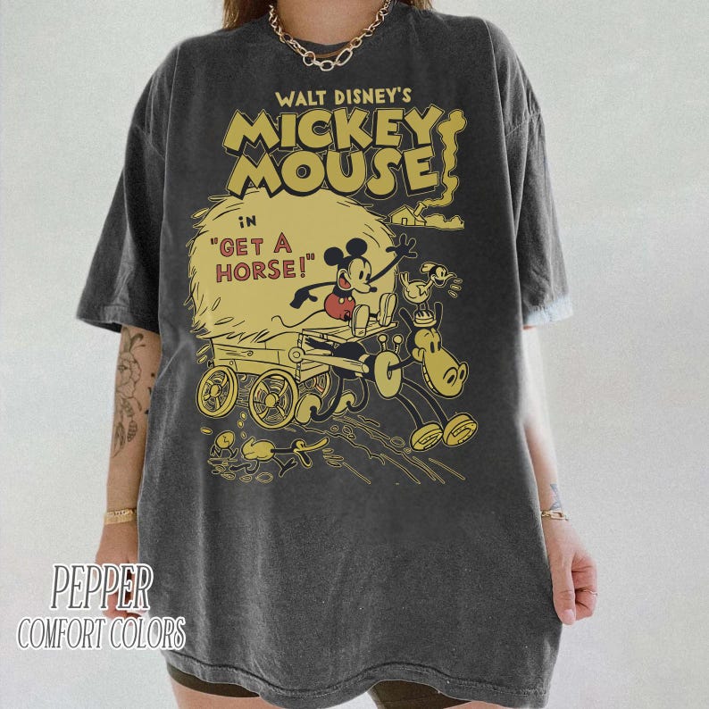 May include: Dark gray t-shirt featuring a vintage Mickey Mouse graphic. The design includes Mickey Mouse in a cart with a horse, with text that reads "WALT DISNEY'S MICKEY MOUSE" and "GET A HORSE!". The shirt is from Pepper Comfort Colors.