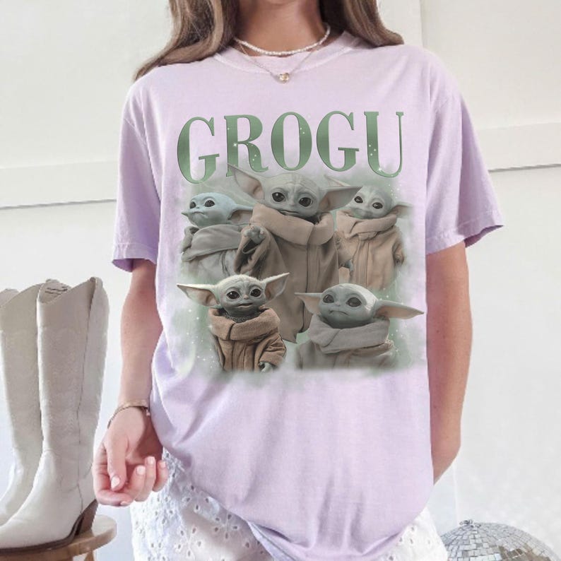 Puede incluir: Una camiseta de color lila claro con la palabra "GROGU" en verde sobre un gr&aacute;fico de Grogu de The Mandalorian. El gr&aacute;fico muestra a Grogu en varias poses. La camiseta tiene mangas cortas.