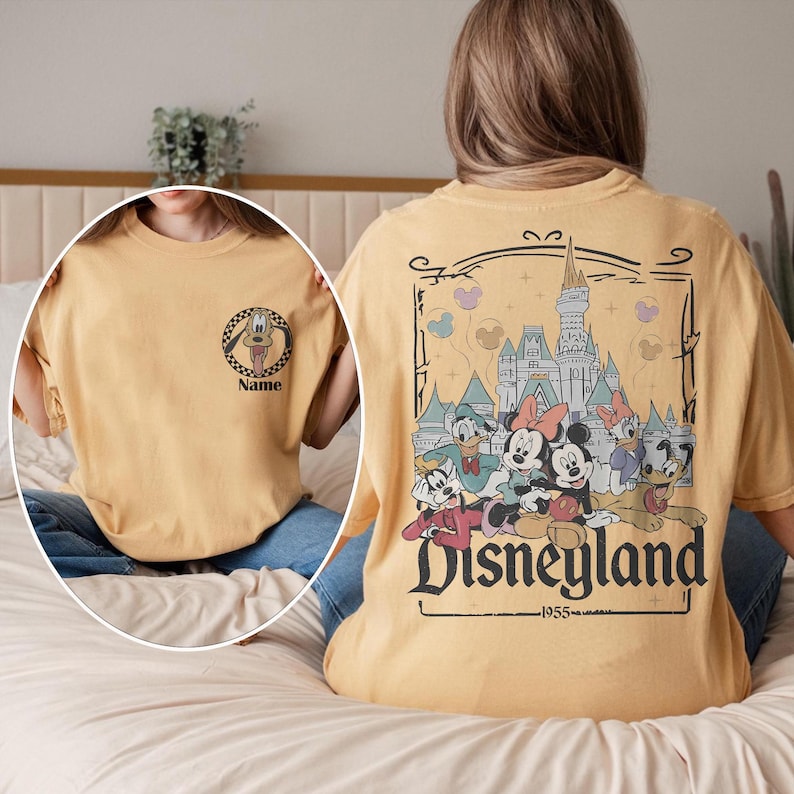 May include: Mustard yellow t-shirt featuring a Disneyland graphic on the back with Mickey Mouse, Minnie Mouse, Donald Duck, and other characters. The front has a Pluto graphic with the word "Name".