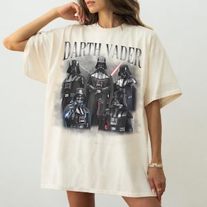 May include: Cream-colored oversized t-shirt featuring a graphic of Darth Vader and other characters from the Star Wars franchise. The text "Darth Vader" is printed across the top. The graphic includes a red lightsaber.