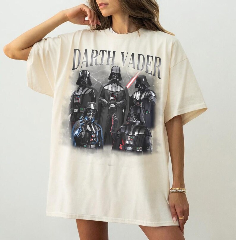 May include: Cream-colored oversized t-shirt featuring a graphic of Darth Vader and other characters from the Star Wars franchise. The text "Darth Vader" is printed across the top. The graphic includes a red lightsaber.
