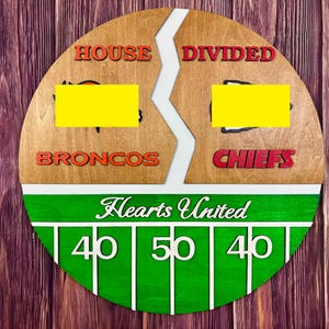 May include: A circular wooden sign featuring a split design with the text HOUSE DIVIDED and the team names BRONCOS and CHIEFS. Below, a green football field graphic displays the text Hearts United with white yard lines and the numbers 40, 50, 40.