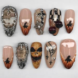 May include: A collection of ten artificial nails with various Halloween-themed designs. The nails feature a range of colors, including nude, orange, black, and silver. Some nails have pumpkin, cross, and skull designs.