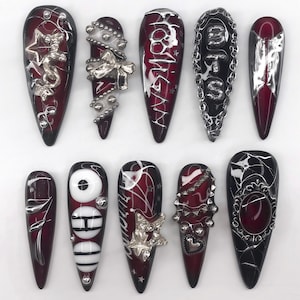 May include: A set of ten stiletto-shaped press-on nails featuring a deep burgundy and black color palette. The designs include silver metallic accents, 3D charms like stars, bows, and hearts, chains, studs, and white text reading HOOD and MTS.
