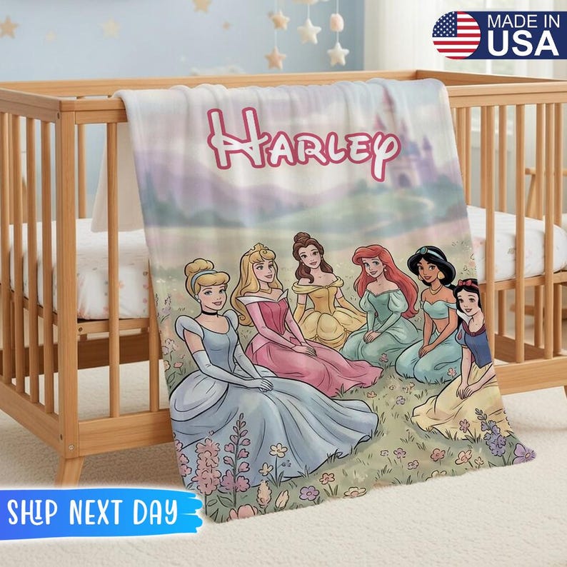 May include: A personalized blanket featuring the name "Harley" in pink script above a scene with Disney princesses. The blanket has a soft, pastel color scheme and is draped over a wooden crib. The words "MADE IN USA" are visible.