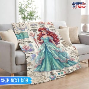 May include: A beige throw blanket featuring a detailed illustration of a mermaid in a teal gown, holding a staff. The blanket includes drawings of seashells, coral, and a map. The blanket is approximately 57 inches long.