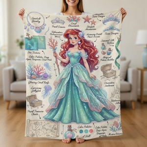 May include: A teal and pink blanket featuring an illustration of a mermaid with red hair and a teal gown. The blanket includes illustrations of seashells, coral, and other ocean-themed accessories. The color palette includes deep aqua, turquoise, and coral pink.
