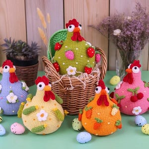 Könnte beinhalten: Eine Sammlung farbenfroher, gehäkelter Hühnerfiguren, jede mit einzigartigen Mustern und Verzierungen. Ein Huhn sitzt in einem Weidenkorb. Dekorative Ostereier sind um die Hühner herum verstreut und schaffen eine festliche Atmosphäre. Die Hühner sind in Blau-, Gelb-, Orange-, Rosa- und Grüntönen gehalten.