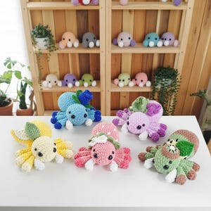 Könnte beinhalten: Eine Sammlung farbenfroher, gehäkelter Oktopus-Plüschtiere. Die Plüschtiere sind in verschiedenen Farben wie Blau, Rosa, Gelb, Grün und Lila gehalten. Einige haben Blumen- oder Blätterakzente. Im Hintergrund ein Holzregal mit weiteren Oktopus-Plüschtieren.