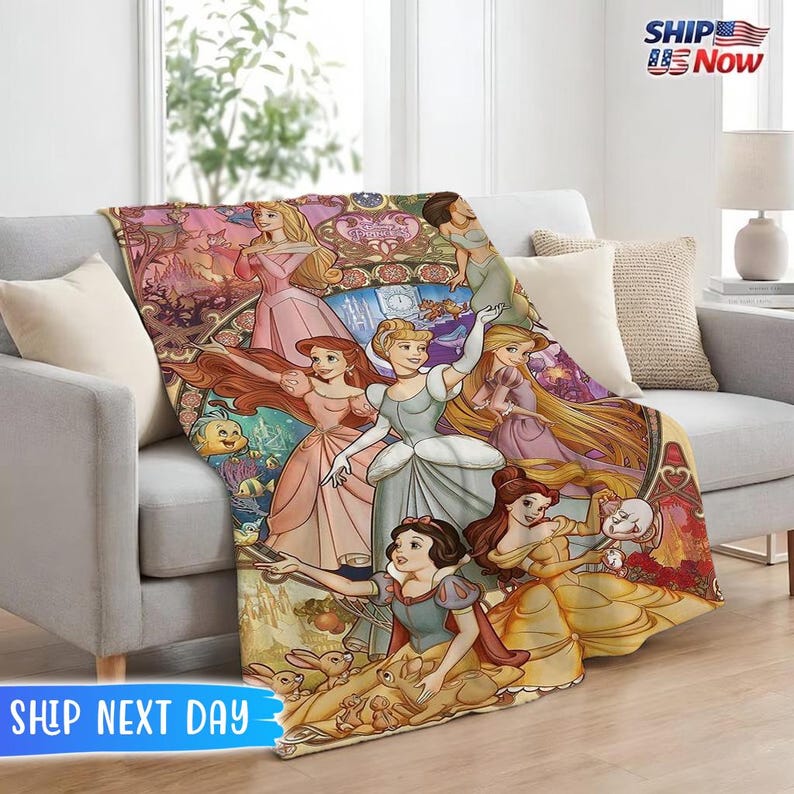 May include: A colorful throw blanket featuring illustrations of several princesses. The blanket has a variety of colors, including pink, blue, yellow, and gold. The blanket is draped over a gray couch.