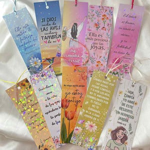 Puede incluir: Un conjunto de coloridos marcadores con citas inspiradoras y diseños florales. Cada marcador presenta un diseño diferente, con texto en español e inglés, y una cinta para facilitar su uso. Los marcadores están hechos de un material brillante y holográfico.