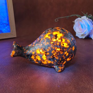 May include: A whale-shaped sculpture made from a speckled blue and orange stone. The sculpture has a smooth, rounded body with a small tail and fins. The orange color gives the impression of glowing light.