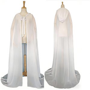 以下が含まれることがあります： マネキンに展示された、長い白いフード付きケープ。ケープは首元にリボン結びがあり、長いトレーンが付いています。生地は軽く、半透明で、わずかな光沢があります。フォーマルな機会に適しています。