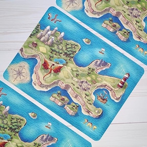 May include: A set of illustrated game cards featuring a fantasy island map with a red dragon, lighthouse, and sailing ships. The cards have a blue ocean background and a compass rose.