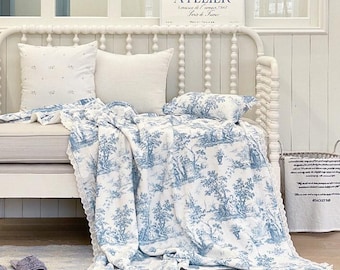 Puede incluir: Un banco blanco con una manta y cojines de toile de Jouy azules y blancos. La manta presenta una escena pastoral detallada. Un pequeño cojín con estampado floral y un cojín blanco están en el banco. Un letrero enmarcado con la palabra "ATELIER" está en la pared.