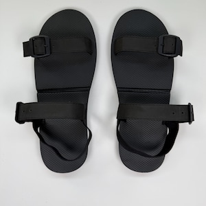 May include: A pair of black sandals featuring adjustable straps and buckle fastenings. The sandals have a textured footbed and a simple design, suitable for casual wear.