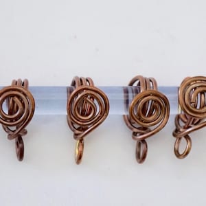 Op de afbeelding: Vier koperen draadringen met een spiraalvormig ontwerp. Elke ring heeft een kleine lus aan de onderkant.