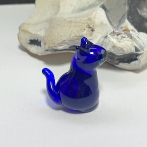 Könnte beinhalten: Eine kleine, kobaltblaue Glaskatzenfigur. Die Katze sitzt mit dem Schwanz um den Körper gewickelt.