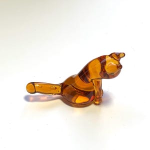 Op de afbeelding: Een klein amberkleurig glazen beeldje van een kat die zit met zijn staart om zijn lichaam gekruld.