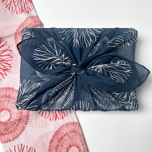 May include: A blue fabric gift wrap with a white floral pattern is tied with a knot. A pink fabric with a red floral pattern is visible in the background.