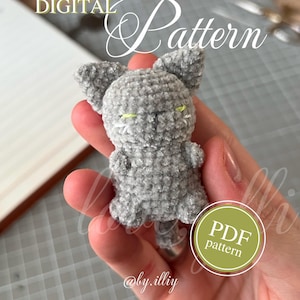 May include: A gray crocheted cat figurine with yellow eyes and a white nose. The image includes the text "DIGITAL Pattern" and "PDF pattern". The pattern is available for sale, as indicated by the text.