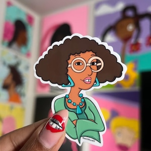 May include: A sticker of a cartoon woman with brown hair, wearing glasses, a green shirt, and a turquoise necklace. The sticker has the text "RaeOfSun83" on the bottom.