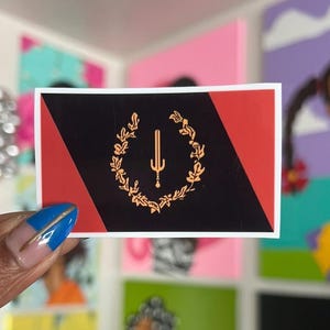 May include: A black and red sticker with a gold emblem featuring a sword and a laurel wreath. The sticker has a diagonal red stripe.