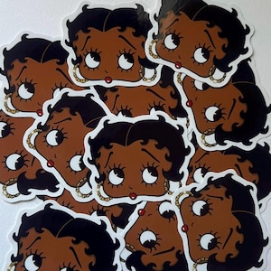 May include: A sheet of stickers featuring multiple cartoon images of a brown-skinned woman with black hair and large eyes. The woman is wearing gold jewelry and has a red lip.