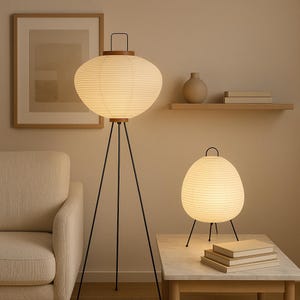 Könnte beinhalten: Eine Stehlampe und eine passende Tischlampe, beide mit runden, gerippten, cremeweißen Papierschirmen, dunklen Holzdetails und dünnen, schwarzen Metall-Dreibeinständern. Die Lampen strahlen ein warmes, sanftes Licht in den Raum aus.