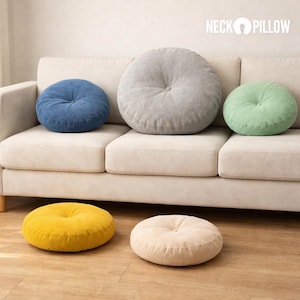 May include: A selection of round cushions in shades of blue, grey, and green are placed on a beige sofa. Two more cushions in yellow and cream are on the wooden floor. Each cushion has a central button.