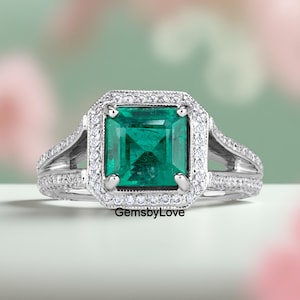 May include: A square-cut emerald ring with a halo of small diamonds. The ring has a split shank design with additional small diamonds. The text "GemsbyLove" is visible on the ring.