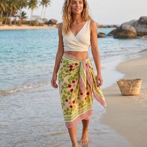 May include: A cream-coloured sleeveless wrap top paired with a sarong featuring a light yellow background, a repeating pattern of red radishes with green leaves, and a red and white striped border tied at the waist with a side knot detail.