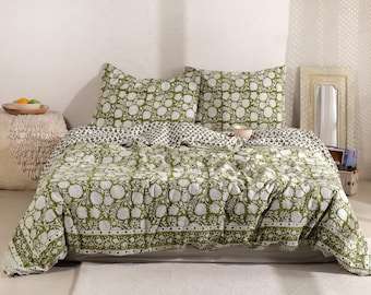 May include: A bed with a green and white floral patterned quilt and matching pillowcases. The quilt features a large floral design, and the pillowcases have a similar pattern. The bed is made up with a white sheet and a white rug is on the floor.