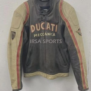May include: A vintage Ducati leather motorcycle jacket in gray, beige, and red. The jacket features the Ducati logo and the words "Meccanica" and "IRSA SPORTS". The jacket has a zipper closure and two front pockets.